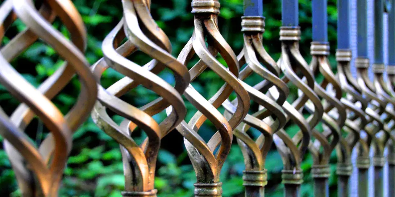 Detailaufnahme eines verzierten metallzauns, der darauf wartet, gestrichen zu werden. Die gedrehten Elemente glänzen im Licht.