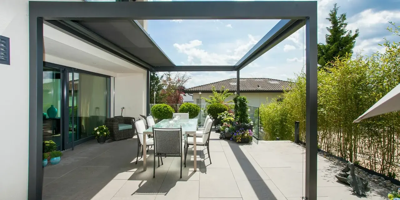 Moderne Terrassenbeschattung Ideen: Ein Essbereich unter einer Pergola mit Glasdach, umgeben von Bambus und Blumen.