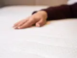 Eine Hand liegt auf einer weißen Matratze. Wann sollte man eine Matratze austauschen? Wenn sie durchgelegen ist oder Flecken hat.