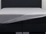 Ein graues Spannbettlaken wird über ein Boxspringbett gezogen. So beziehe ich ein Boxspringbett – einfach und schnell.