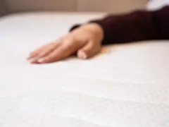Eine Hand liegt auf einer weißen Matratze. Wann sollte man eine Matratze austauschen? Wenn sie durchgelegen ist oder Flecken hat.
