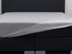 Ein graues Spannbettlaken wird über ein Boxspringbett gezogen. So beziehe ich ein Boxspringbett – einfach und schnell.
