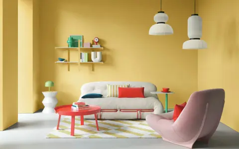 Lebendige wohnraumgestaltung farben: gelbe Wände, ein flauschiges Sofa, ein roter Couchtisch und ein rosa Sessel schaffen eine fröhliche Atmosphäre.