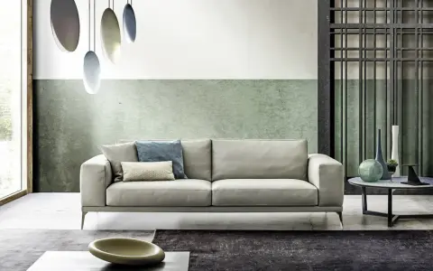 Modernes Wohnzimmer mit hellem Sofa, grüner Wand und stilvollem farbkonzept. Hängende Lampen und dekorative Vasen ergänzen das Ambiente.