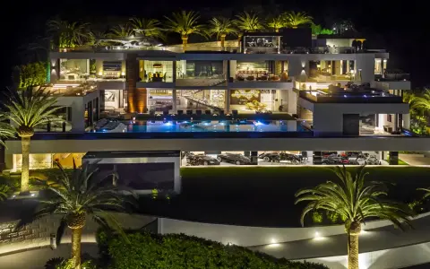 Luxuriöse Villa bei Nacht mit Pool, Palmen und einer Garage voller teuerstes Holz der Welt.