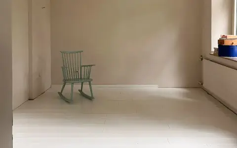 Ein hell gestrichener holzboden mit einer mintgrünen Schaukelstuhl.