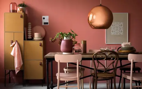 Ein Esszimmer mit altrosa Wänden. Ein kupferfarbener Lampenschirm und ein Holzmöbelstück mit gelben Türen. Welche Farbe zu altrosa? Zarte Rosatöne und Erdtöne passen gut.