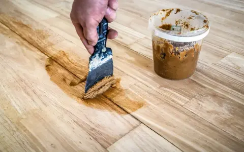 Mit einem Spachtel und Holzpaste werden Kratzer aus einem Holztisch entfernt.