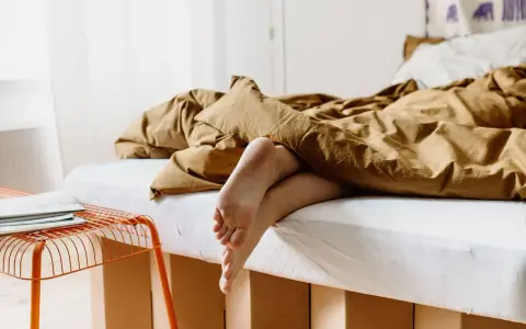 Füße ragen aus einem gemütlichen, braunen Bett hervor. Das Bett ist 210 cm lang und lädt zum Entspannen ein.