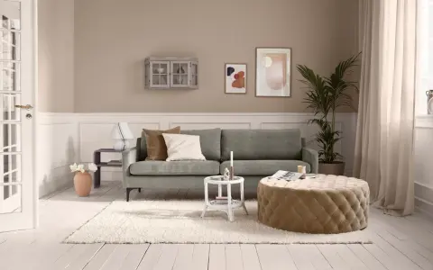 Ein Wohnzimmer mit salbeigrünem Sofa. Braune und cremefarbene Kissen, ein beiger Hocker und eine helle Wand zeigen, welche Farbe passt zu Salbei.