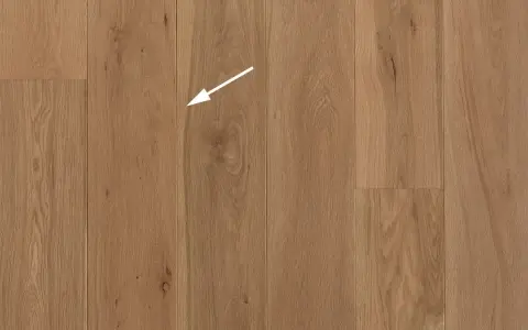 Holzboden mit natürlicher Maserung. Ein weißer Pfeil zeigt auf eine kleine Astloch-Stelle im splint holz.