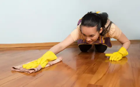 Frau mit gelben Handschuhen reinigt glänzenden Holzboden. Sorgfältige holzboden pflege für ein schönes Zuhause.