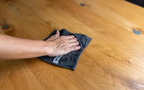 Hand wischt mit Tuch über Holzoberfläche, um schwarze Flecken zu entfernen. Hausmittel-Tipp für sauberes Holz.