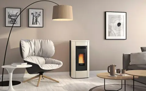 Gemütliches Wohnzimmer mit modernem Pellet-Kaminofen. Die warme wandfarbe hinter kaminofen harmoniert mit dem cremefarbenen Ofen und dem bequemen Sessel.
