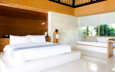 Luxuriöses Schlafzimmer mit einem großen weißen Bett, das den Unterschied zwischen einem King und Queen Bett verdeutlicht. Holzakzente und viel Licht.