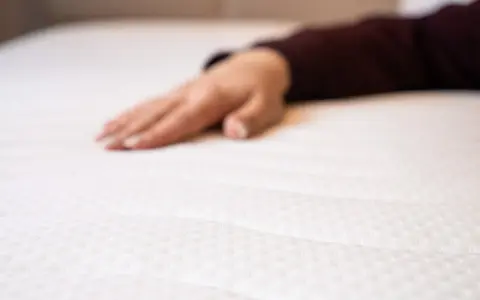 Eine Hand liegt auf einer weißen Matratze. Wann sollte man eine Matratze austauschen? Wenn sie durchgelegen ist oder Flecken hat.