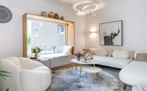Modernes Wohnzimmer mit weißem Sofa, gemütlichem Sessel und einem Fensterplatz. Die schale dekorieren modern mit Vasen und Büchern.