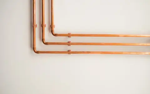 Kupferrohre an einer weißen Wand, die sich in einem rechten Winkel biegen. Tolle rohrverkleidung ideen für ein industrielles oder modernes Design.