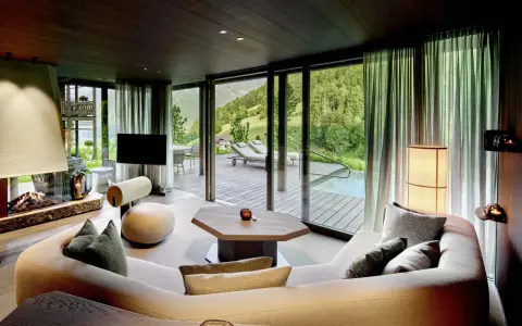 Gemütliches Wohnzimmer mit Kamin, großem Sofa und Bergblick. Die luxuriöse Chalet-Inneneinrichtung strahlt Wärme und Eleganz aus.