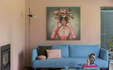 Ein blauer Sofa mit Kissen vor einer Wand mit einem surrealen Gemälde, das eine Frau mit Blumen und Schmetterlingen auf dem Kopf zeigt. Eine kreative Wandgestaltung, die zum Träumen einlädt.