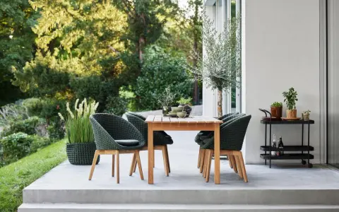 Einladende Sitzgruppe auf einer modernen Terrasse, perfekt für die nächste terrasse renovieren. Grüne Korbsessel und Holztisch laden zum Verweilen ein.