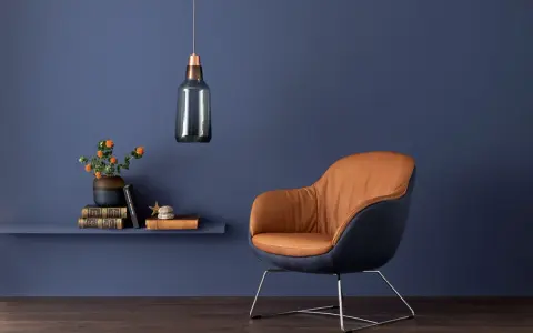 Ein Sessel mit braunem Leder und dunkelblauem Stoff vor einer blauen Wand. Orange Blumen auf einem Regal zeigen, welche Farbe passt zu Blau.