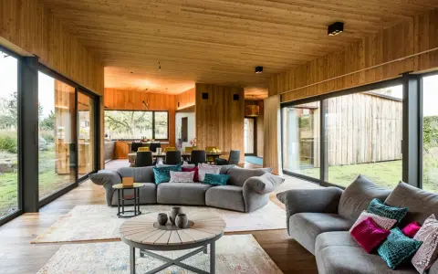 Gemütliches Wohnzimmer mit holzverkleideten Wänden und Decke, das zeigt, wie man eine holzdecke modern gestalten kann. Große Fensterfronten bieten Blick ins Grüne.