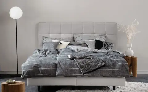 Stilvolle Schlafzimmer Ideen mit einem grauen Boxspringbett, gestreifter Bettwäsche und modernen Akzenten.