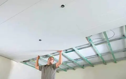 Mann verkleidet die Decke mit Gipskartonplatten. Die Unterkonstruktion ist sichtbar.