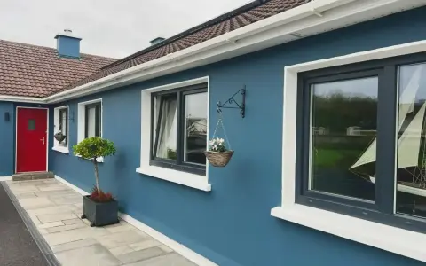 Ein blaues Haus mit roten Tür und dunklen Kunststofffenstern. Die Fensterrahmen sind in einem eleganten Anthrazit gehalten, was die modernen Kunststofffenster Farben unterstreicht.