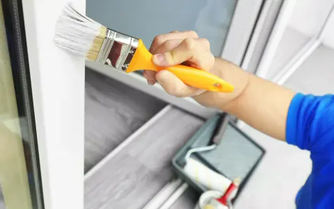 Mit welcher Farbe kann man Kunststoff streichen? Ein Pinsel mit weißer Farbe wird auf einen weißen Kunststoffrahmen aufgetragen.