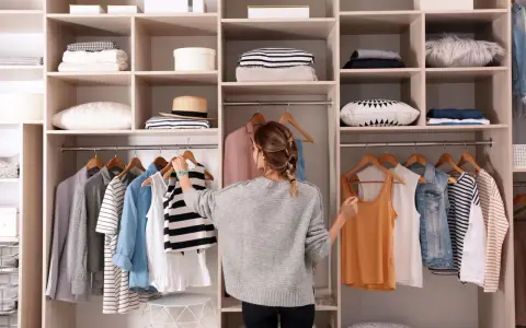 Frau sortiert Kleidung in einem offenen Schrank. Sie überlegt, was sie anziehen soll, um den offenen Schrank zu verkleiden.