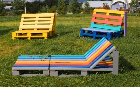 Bunte Palettenmöbel im Garten: Eine gelbe Bank, eine mehrfarbige Sitzbank und eine bunte Liege laden zum Entspannen ein. Paletten streichen ohne schleifen ist hier die Devise.