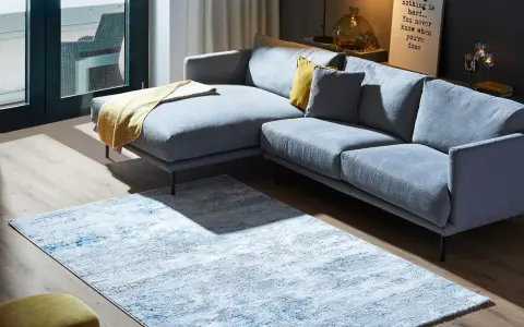Ein moderner Wohnbereich mit einem grauen Ecksofa und einem Teppich, der richtig platziert unter dem Sofa liegt.