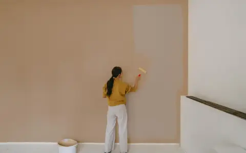 Frau streicht Wand mit neuer Farbe. Man fragt sich, wie lange braucht wandfarbe zum trocknen, während die alte Farbe noch sichtbar ist.