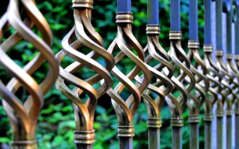 Detailaufnahme eines verzierten metallzauns, der darauf wartet, gestrichen zu werden. Die gedrehten Elemente glänzen im Licht.