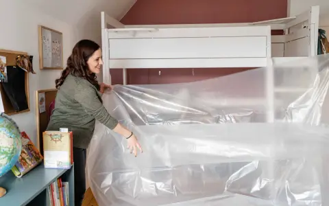Frau bereitet eine Matratze vor, um sie zu vakuumieren. Sie zieht die Plastikfolie über das Bett.