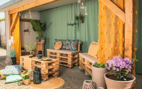 Gemütliche Sitzecke im Hof gestalten mit Palettenmöbeln, bunten Kissen und Lichterkette. Einladend und stilvoll.
