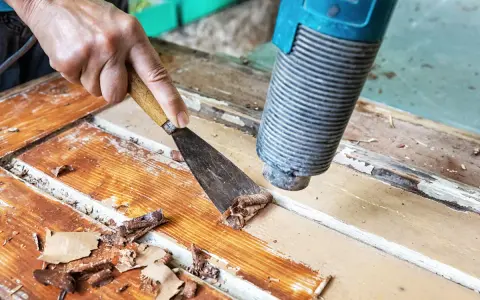 Farbe von Holz entfernen ohne Schleifen: Heißluftföhn und Spachtel lösen alte Lackschichten von einer Holztür.