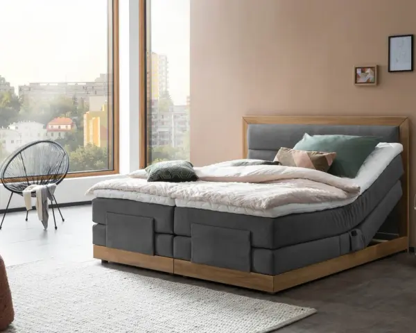 Modernes Boxspringbett mit Holzrahmen und grauem Stoffbezug. Die Matratze wirkt etwas zu hart, aber die Kissen laden zum Entspannen ein.