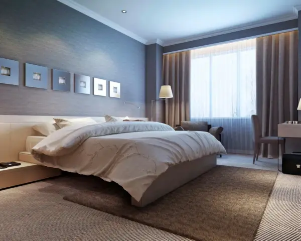 Modernes Schlafzimmer mit einem bequemen Bett, das wie ein wasserbett oder boxspringbett wirkt. Dekorative Wandbilder und ein Schreibtisch mit Lampe.