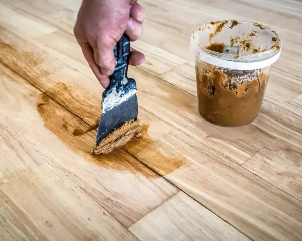 Mit einem Spachtel und Holzpaste werden Kratzer aus einem Holztisch entfernt.