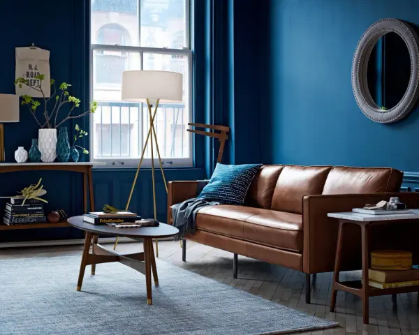 Gemütliches Wohnzimmer mit tiefblauen Wänden, brauner Ledercouch und einem hellblauen Teppich. Die Kombination aus Blau und Braun schafft eine warme Atmosphäre.