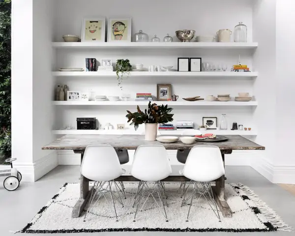 Moderne Esszimmer Wand Ideen: Weiße Regale voller Deko, Geschirr und Bilder über einem rustikalen Holztisch mit weißen Stühlen.