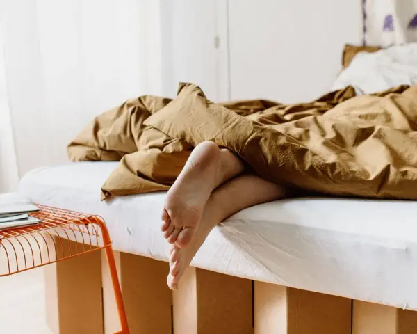 Füße ragen aus einem gemütlichen, braunen Bett hervor. Das Bett ist 210 cm lang und lädt zum Entspannen ein.