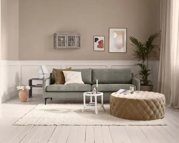 Ein Wohnzimmer mit salbeigrünem Sofa. Braune und cremefarbene Kissen, ein beiger Hocker und eine helle Wand zeigen, welche Farbe passt zu Salbei.