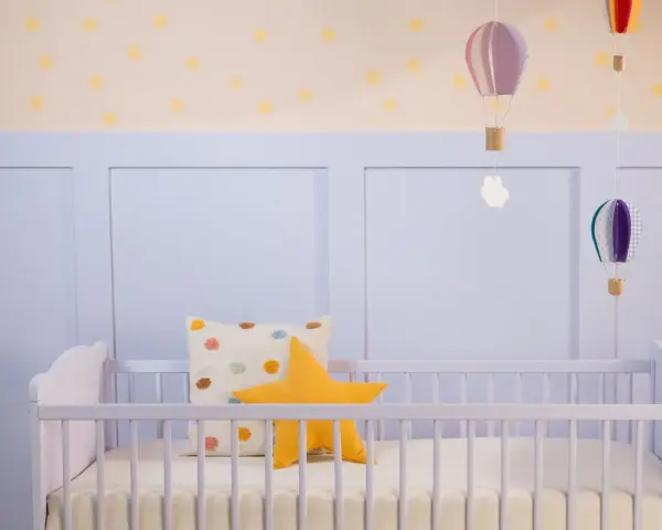 Ein frisch gestrichenes Kinderbett in zartem Lila, dekoriert mit bunten Kissen und schwebenden Heißluftballons.