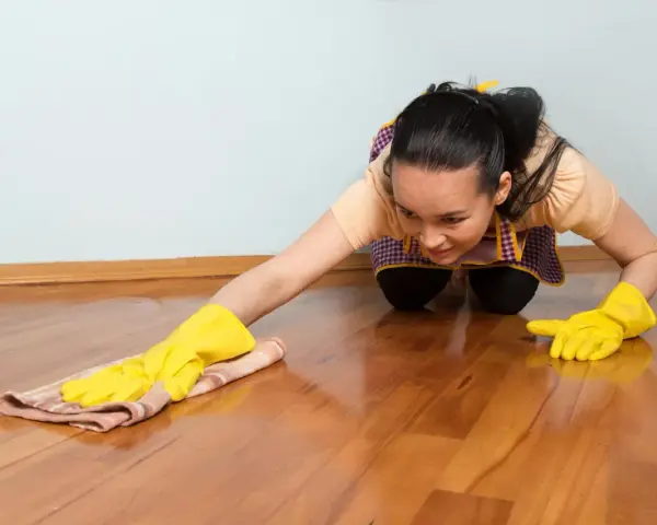 Frau mit gelben Handschuhen reinigt glänzenden Holzboden. Sorgfältige holzboden pflege für ein schönes Zuhause.