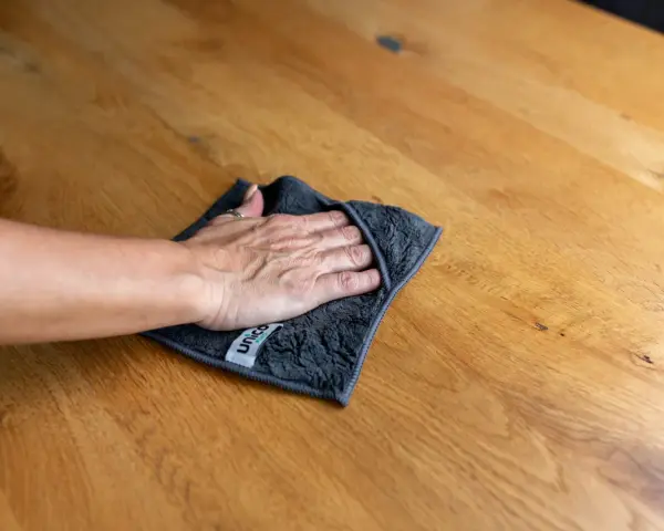 Hand wischt mit Tuch über Holzoberfläche, um schwarze Flecken zu entfernen. Hausmittel-Tipp für sauberes Holz.