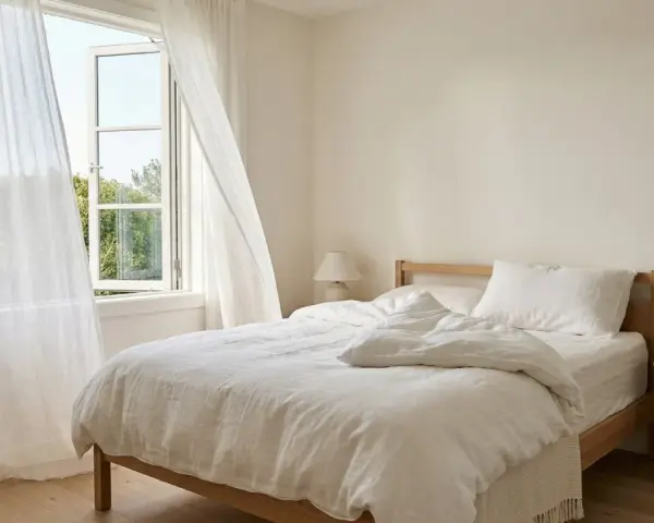 Ein helles Schlafzimmer mit offenem Fenster und weißen Vorhängen. Auf dem Nachttisch steht ein Thermometer, das die angenehme schlafzimmer temperatur anzeigt.